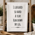 White kitchen towel with I Laughed So Hard A Tear Ran Down My Leg text displayed on a wooden ladder rack