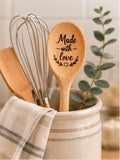 Engraved wooden spoon with Made with Love text and heart laurel detail in a ceramic utensil holder with greenery