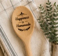 Engraved wooden spoon with Happiness is Homemade text and leaf detail on a linen background with greenery