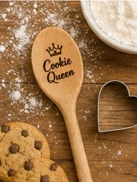 Engraved wooden spoon with Cookie Queen and crown design on a rustic wooden surface with cookies