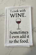 White kitchen towel with I Cook With Wine text and red wine glass illustration on a marble countertop